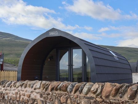 An arched pod cabin with glass doors behind a stone wall in a rural landscape at Woodpecker in Chapel Le Dale near Ingleton