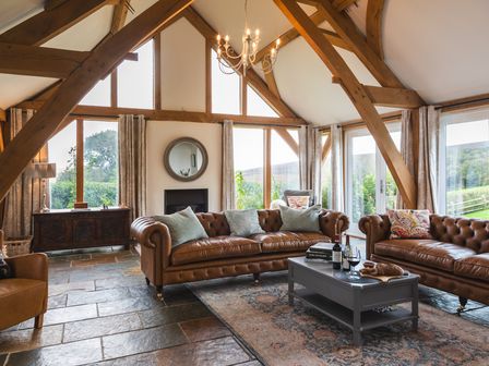 A living room with leather sofas a coffee table and wooden beams at The Farmhouse at Broad Downs in Malborough