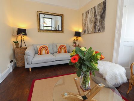 A living room with a gray sofa orange pillows a glass coffee table with flowers and a side table with lamps at Belmont House in Bowness-On-Windermere
