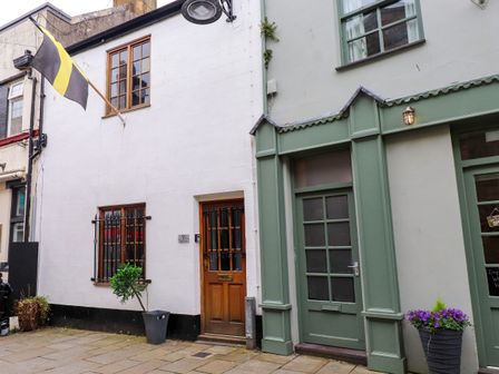 Two adjacent buildings with one white and one green facade a black and yellow flag and potted plants outside at Hole in the Wall in Caernarfon