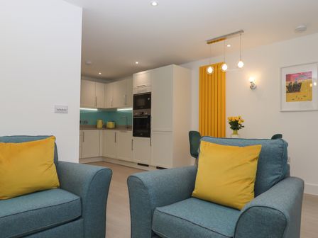 A living room with blue armchairs with yellow cushions and a kitchen with white cabinets and turquoise backsplash at Rolles Rainbow in Exmouth