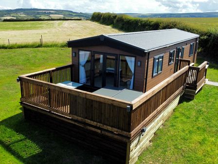 A wooden cabin with a fenced deck surrounded by grass and fields at Aspen Lodge in Whitby