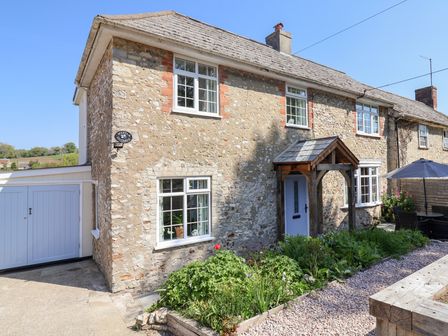 A stone cottage with white windows a wooden porch and garden in front at Myrtle Cottage in Uplyme