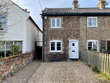 A stone cottage with a white door and windows and a gravel driveway at Caines Cottage in Westleton