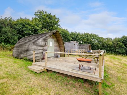 Wooden pods with a deck and picnic tables in a grassy area surrounded by trees at Hen House @ Penbugle Organic Farm in St Keyne near Duloe