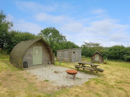 An outdoor area with wooden cabins a picnic table and a fire pit at Pig Pen @ Penbugle Organic Farm in St Keyne near Duloe