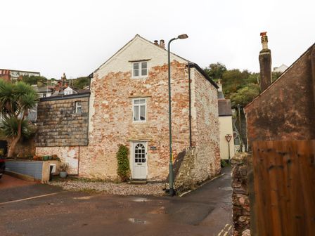 A stone house with a white door and two windows beside a street lamp and palm trees at 3 Pebble Cottage in Brixham