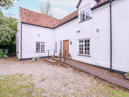 An exterior view of a white house with a wooden door and multiple windows and a gravel driveway at White House Cottage in Little Snoring near Fakenham