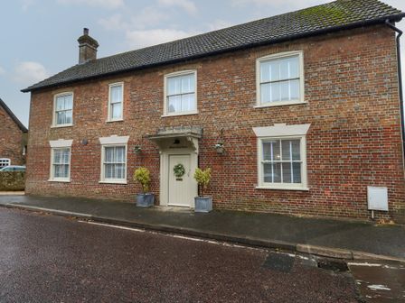 A brick house with six windows and a central door with plants on the pavement at Manor Farm House in Bere Regis