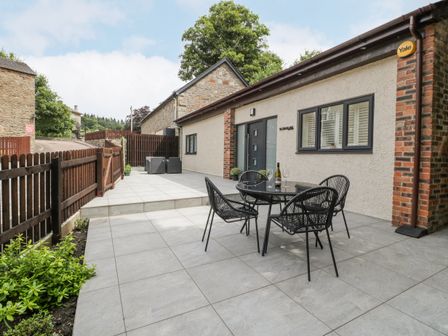 An outdoor tiled patio area with a black table and four chairs and a seating area near a white building at The Fountain Lodge in Parkend