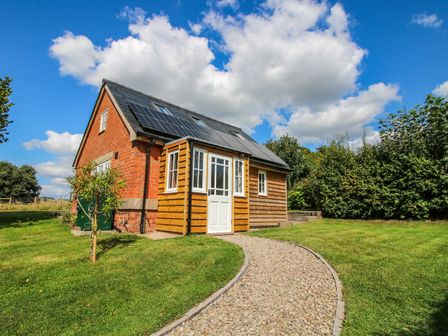 A small house with solar panels on the roof and a gravel pathway in a grassy yard at Rose Cottage in Garway