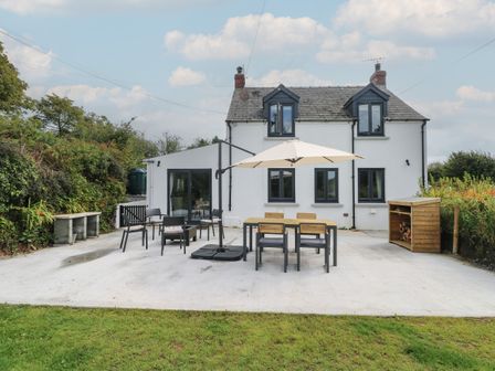 A white two-story house with outdoor dining table chairs and umbrella at Folly Cottage Llanteg near Saundersfoot