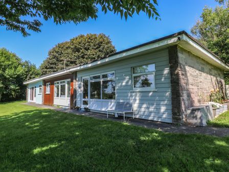 A single-story house with a bench and potted plants outside surrounded by trees at 61 Norton Park in Dartmouth