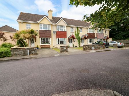 A row of beige townhouses with small front gardens and parked cars at 23 Cois Caol in Skibbereen County Cork