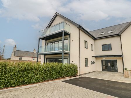 An exterior view of a multi-story building with glass balconies and a paved driveway at Glynllifon 1 in Marian-glas near Benllech