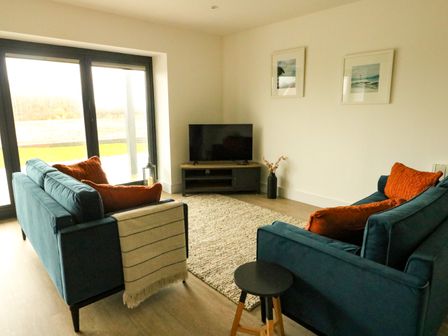 A living room with two blue sofas and orange cushions a rug a TV on a stand and two framed pictures on the wall at Glynllifon 2 in Benllech
