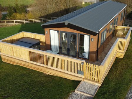 A single-story wooden lodge with a fenced wooden deck and a hot tub on the deck at Juniper Lodge in Whitby