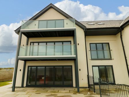 The rear exterior of a modern multi-level house with balconies glass railings and large windows at Glynllifon 3 in Benllech