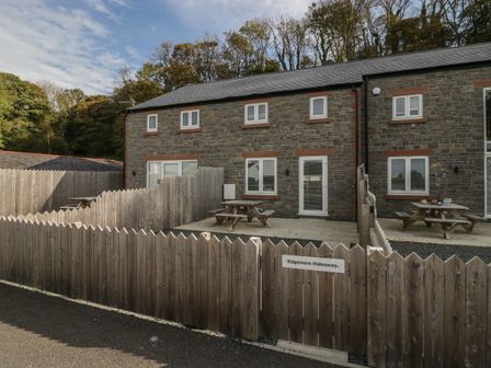 A stone building with wooden fences and picnic tables outside at Edgemere Hideaway in Cartmel