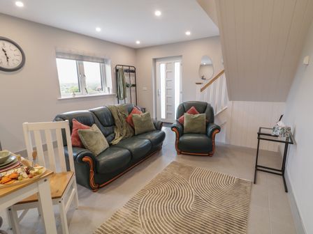 A living room with green leather sofa and armchair cushions rug and dining table at ARD NA GHAOITHE in Loughanure County Donegal