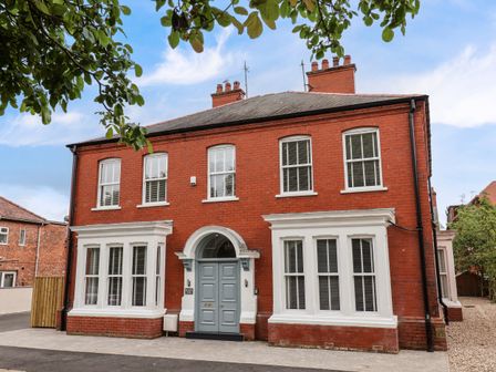 A red brick building with white window frames and a blue double door entrance surrounded by trees at Broad Bay Lodge in Bridlington