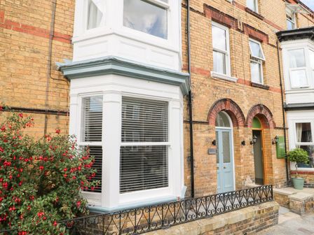 The front exterior of a brick house with a blue door a bay window and a small garden with red flowers at Seascape Villa in Filey