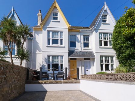 A white terraced house with a yellow front door and blue front door with seating area and palm tree in front at Sea Candy in St Ives