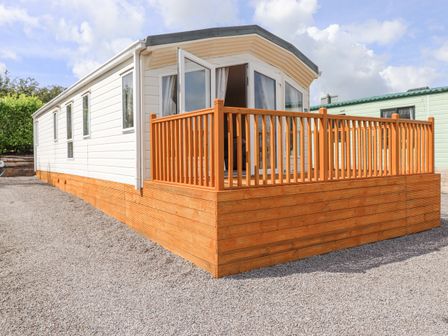 A white mobile home with a wooden deck and railing on a gravel surface at 31 Forest Views in Moota near Aspatria