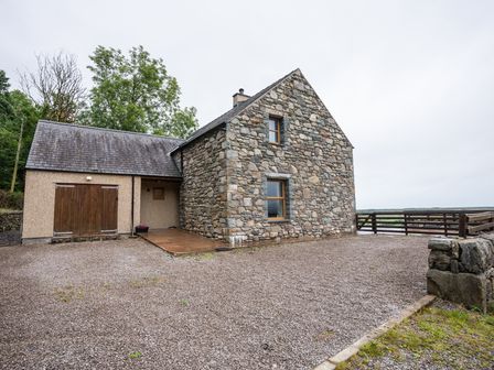 A stone house with a gravel driveway and wooden gate in a rural setting at Carreg Wen in Harlech