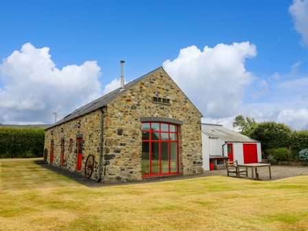 A stone building with red windows and doors and a lawn with a table and chairs at West Dairy near Newport Pembrokeshire