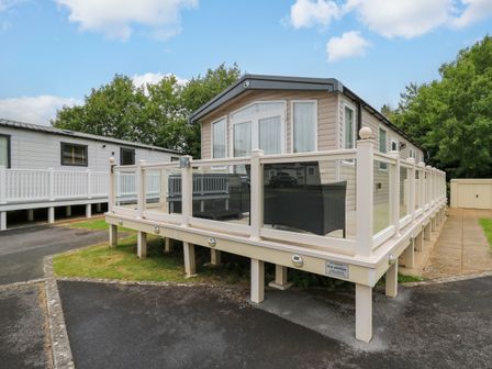 A beige mobile home with a glass and white railing deck and outdoor seating at Osprey 7 in Tenby