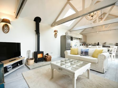 An open living space with a sofa yellow cushions coffee table and wood burning stove at East Farm Croft in Embleton