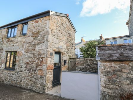 Stone exterior of a building with a dark door and windows next to a white wall and a wooden gate at The Old Dairy Barn in St Just