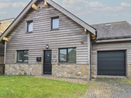 A house with wooden siding and stone foundation a black door with number 2 and a garage door at Dunes in Rhosneigr