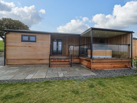 An outdoor view of a wooden cabin with glass doors and a covered patio with a hot tub at Math Lodge 3 Llanelidan near Corwen