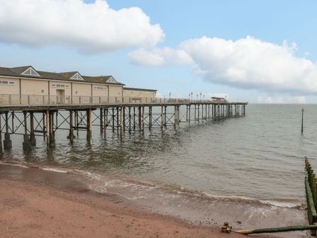 A wooden pier extending over the sea next to a sandy beach at Regents Deck in Teignmouth