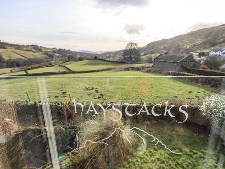 A view of green fields and hills with a stone wall and a barn in the background at Haystacks in Troutbeck