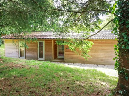 A wooden house with three glass doors surrounded by trees and grass at 10 Waters Edge in Lanreath