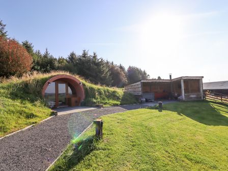 A hobbit style earth house entrance and wooden shelter in a grassy yard at Cae Bach in Cyffylliog near Ruthin