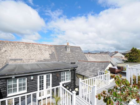 A rooftop terrace with white railing and outdoor furniture overlooking neighboring rooftops at Stones Throw Cottage in Launceston