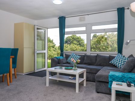 A living room with a large grey sofa blue cushions white coffee table and glass door open to garden at Florences Nest in Dartmouth