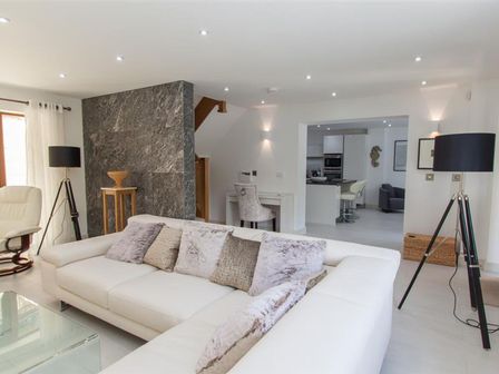 A living room with a white sofa and throw pillows a stone wall a wooden side table a white chair and two black tripod floor lamps at The Arthouse in Ambleside