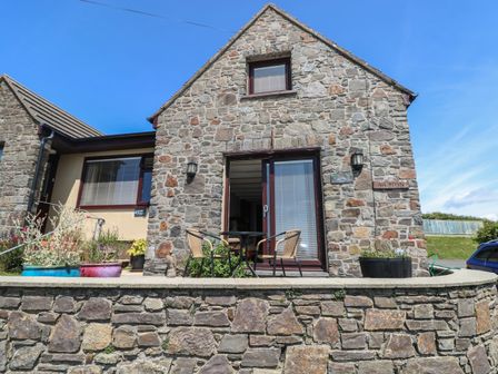 A stone house with a small patio table and two chairs in front of sliding glass doors at Carreg Ddu in Solva