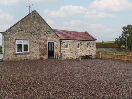 A stone house with a red tiled roof a black door and a gravel yard at Honeysuckle Cottage in Crookham near Coldstream