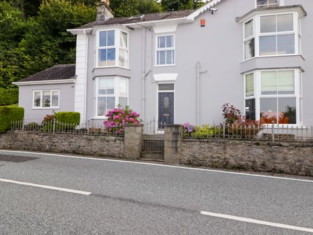 Exterior of a gray house with bay windows a black front door and stone wall with flowering plants at Morva in New Quay