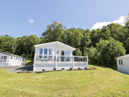 A white cabin with a deck and outdoor furniture surrounded by grass and trees at Bethany's Retreat in Wemyss Bay