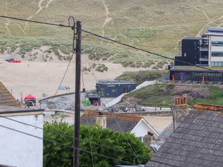 A view of rooftops with a beach and sand dunes in the background at Small Hillman in Perranporth