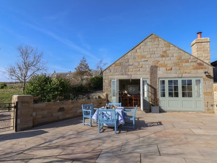 An outdoor patio area with blue chairs and a table set for dining next to a stone building with open doors at Roding Cottage in Egton