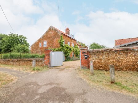 A view of a brick house behind a stone wall and open gate with a driveway at Malthouse Farm in Heacham