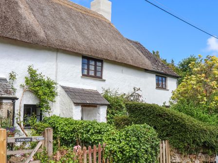 Exterior of a white cottage with thatched roof surrounded by greenery and wooden gates at 2 Freeland Cottages in Manaton near Moretonhampstead